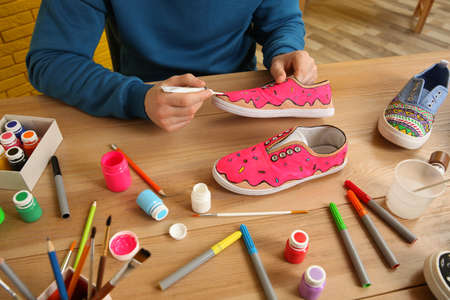Man painting on sneaker at wooden table indoors, closeup. custom shoesの写真素材