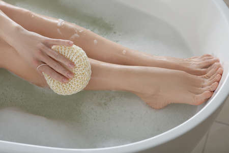 Woman rubbing her leg with sponge while taking bath, closeupの写真素材
