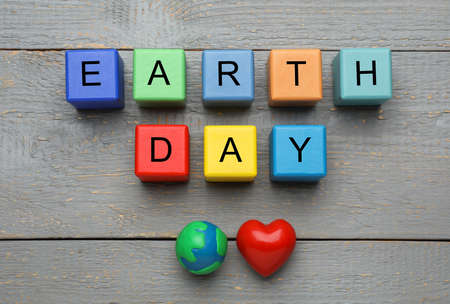 Colorful cubes with words Earth Day, plastic planet and decorative heart on gray wooden table, flat...