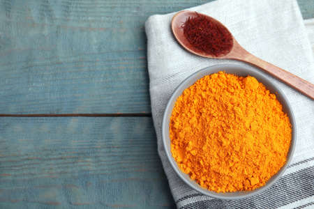 Bowl of saffron powder and spoon with dried flower stigmas on light blue wooden table, flat lay. Space for textの写真素材