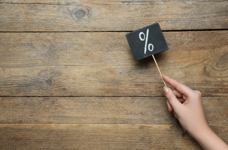 Woman holding sign with percent symbol on wooden background, top view. Space for text