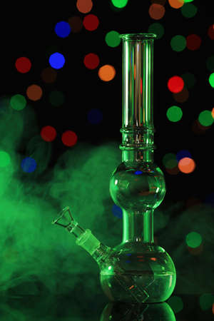 Glass bong with smoke against blurred lights, toned in green. smoking deviceの写真素材