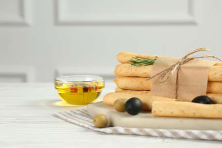 Tasty grissini with rosemary, olives and oil on white wooden table