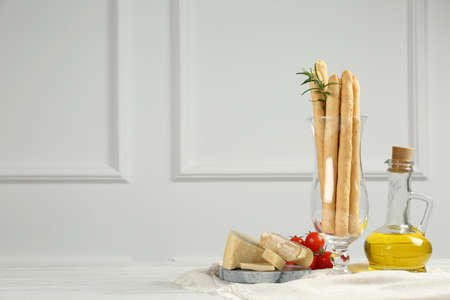 Tasty grissini with oil, tomatoes and cheese on white wooden table, space for textの写真素材
