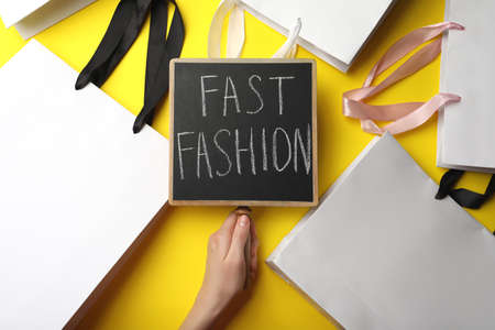 Woman holding small chalkboard with phrase Fast Fashion and white shopping bags on yellow background, top viewの写真素材