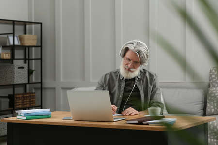 Middle aged man with laptop and headphones learning at table indoors