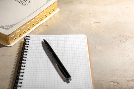 Notebook with pen and old hardcover Bible on gray table. religious book