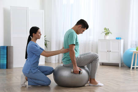 Orthopedist helping patient to do exercise with dumbbell in clinic. scoliosis treatment
