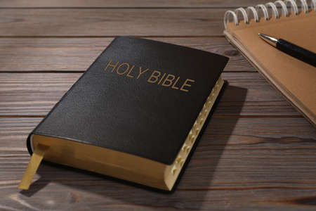 Old hardcover Bible and notebook with pen on wooden table. religious book
