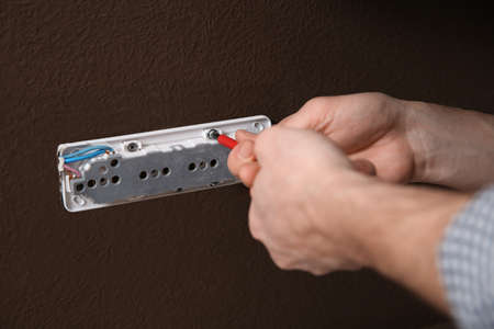 Electrician with screwdriver repairing power socket, closeup
