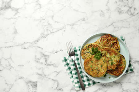 Delicious zucchini fritters served on white marble table, flat lay. Space for text