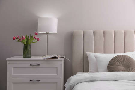 Stylish lamp, flowers and magazine on bedside table indoors. bedroom interior elements
