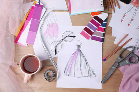 Sketches of clothes and different stuff on wooden table, flat lay. Fashion designer's workplaceの写真素材