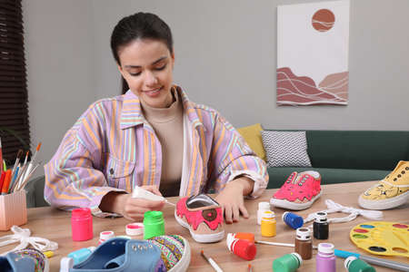 Woman painting on sneaker at wooden table indoors. custom shoes