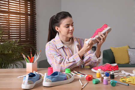 Woman painting on sneaker at wooden table indoors. custom shoesの写真素材