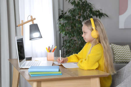 Cute little girl with modern laptop studying online at home. e-learning