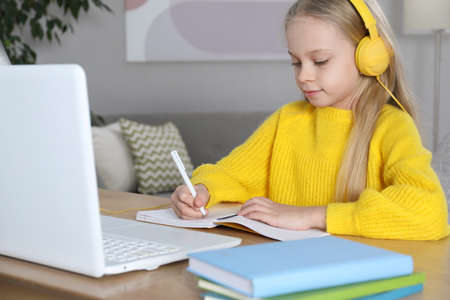 Cute little girl with modern laptop studying online at home. e-learning