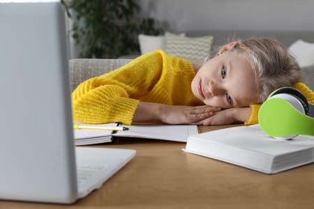 Cute little girl with modern laptop studying online at home. e-learning