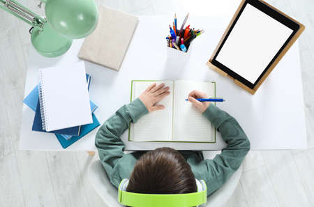 Cute little boy with modern tablet studying online at home, top view. e-learning