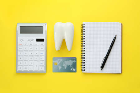 Flat lay composition with ceramic model of tooth and credit card on yellow background. Expensive treatmentの写真素材