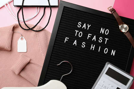 Black letter board with phrase SAY NO TO FAST FASHION, clothes, wristwatch, shopping bags, hanger and calculator on pink background, flat layの写真素材