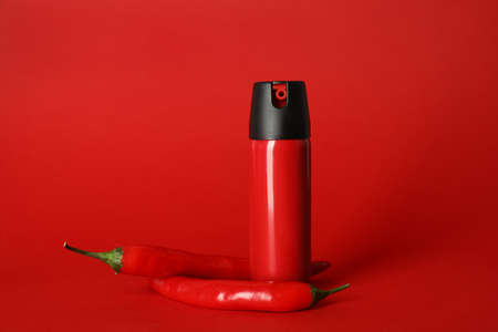 Bottle of gas pepper spray and fresh chili peppers on red backgroundの写真素材