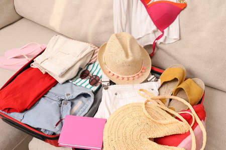 Open suitcase with different women clothes and accessories on sofaの写真素材