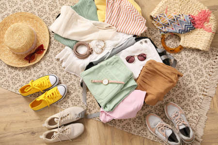 Open suitcase full of clothes and summer accessories near shoes on floor, top viewの写真素材