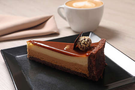 Piece of delicious cheesecake with caramel and chocolate candy on table, closeup