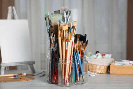 Glass jars with many different paintbrushes on white wooden table indoorsの写真素材