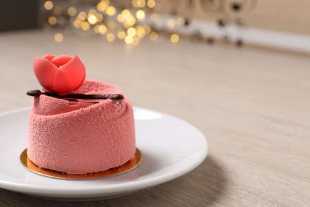 Delicious mousse cake with floral decor on white wooden table against blurred lights, closeup. Space for textの写真素材