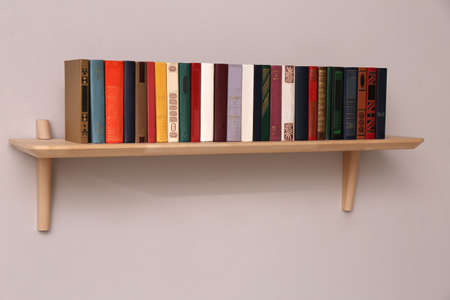 Wooden shelf with different books on light wallの写真素材