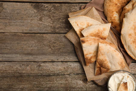 Pieces of fresh pita bread and cream cheese on wooden table, flat lay. Space for text