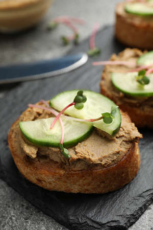 Slices of bread with delicious pate, cucumber and microgreens on gray table, closeup