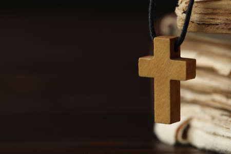 Wooden Christian cross and old books on dark table, closeup. Space for textの写真素材