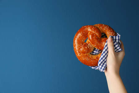 Woman with tasty freshly baked pretzel on blue background, closeup. Space for textの写真素材