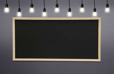 Glowing light bulbs and blackboard hanging on gray wallの写真素材