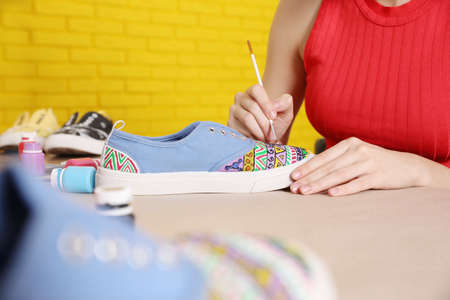Woman painting on sneaker at wooden table indoors, closeup. custom shoesの写真素材