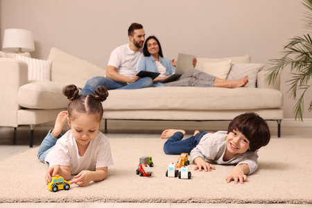 Cute children playing with toys while parents using gadgets on sofa in living roomの写真素材