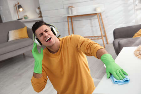 Man in headphones with rag singing while cleaning at homeの写真素材