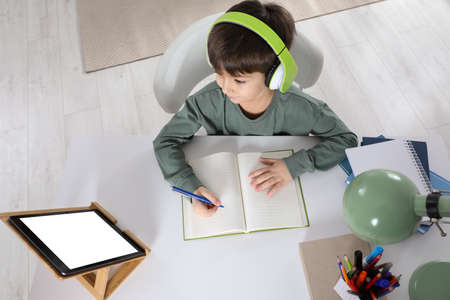 Cute little boy with modern tablet studying online at home, above view. e-learning