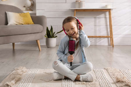 Cute little girl in headphones with hairbrush singing at homeの写真素材