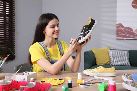 Woman painting on sneaker at wooden table indoors. custom shoesの写真素材