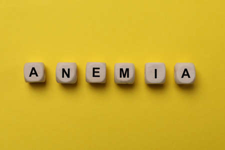Word Anemia made with wooden cubes on yellow background, flat layの写真素材