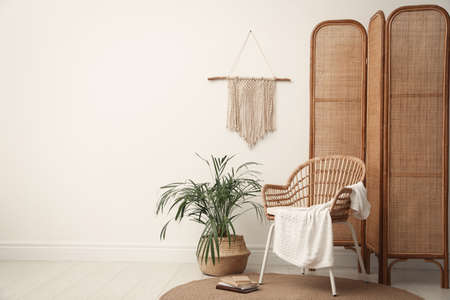 Stylish wooden chair, folding screen and beautiful houseplant near white wall in room. Space for textの写真素材