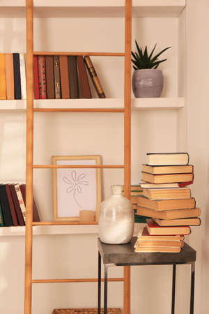 Stack of different books and vase on table near bookshelves in home libraryの写真素材