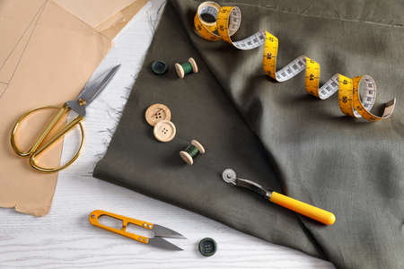 Set of sewing supplies and accessories with fabric on white wooden table, above view