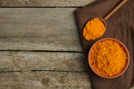 Bowl and spoon with saffron powder on wooden table, top view. Space for text