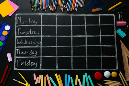 Many different stationery and drawn weekly school timetable on black chalkboard, flat layの写真素材