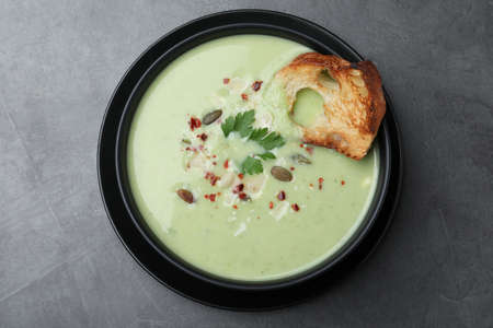 Bowl of delicious asparagus soup on dark table, top view